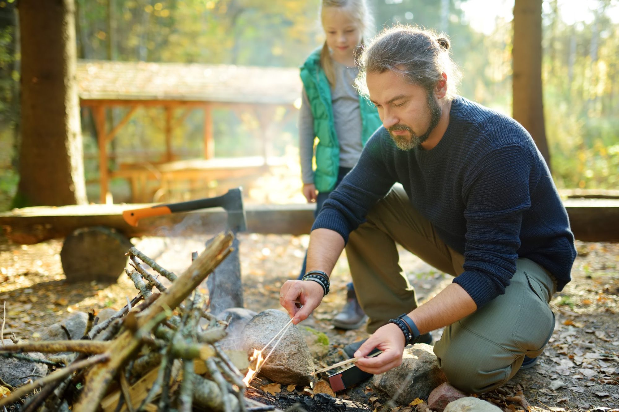 A dad building a fire with his daughter watching.