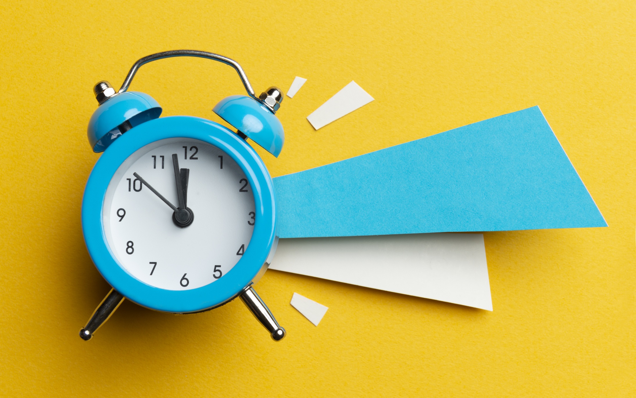 Alarm clock and colour papers on the yellow background.