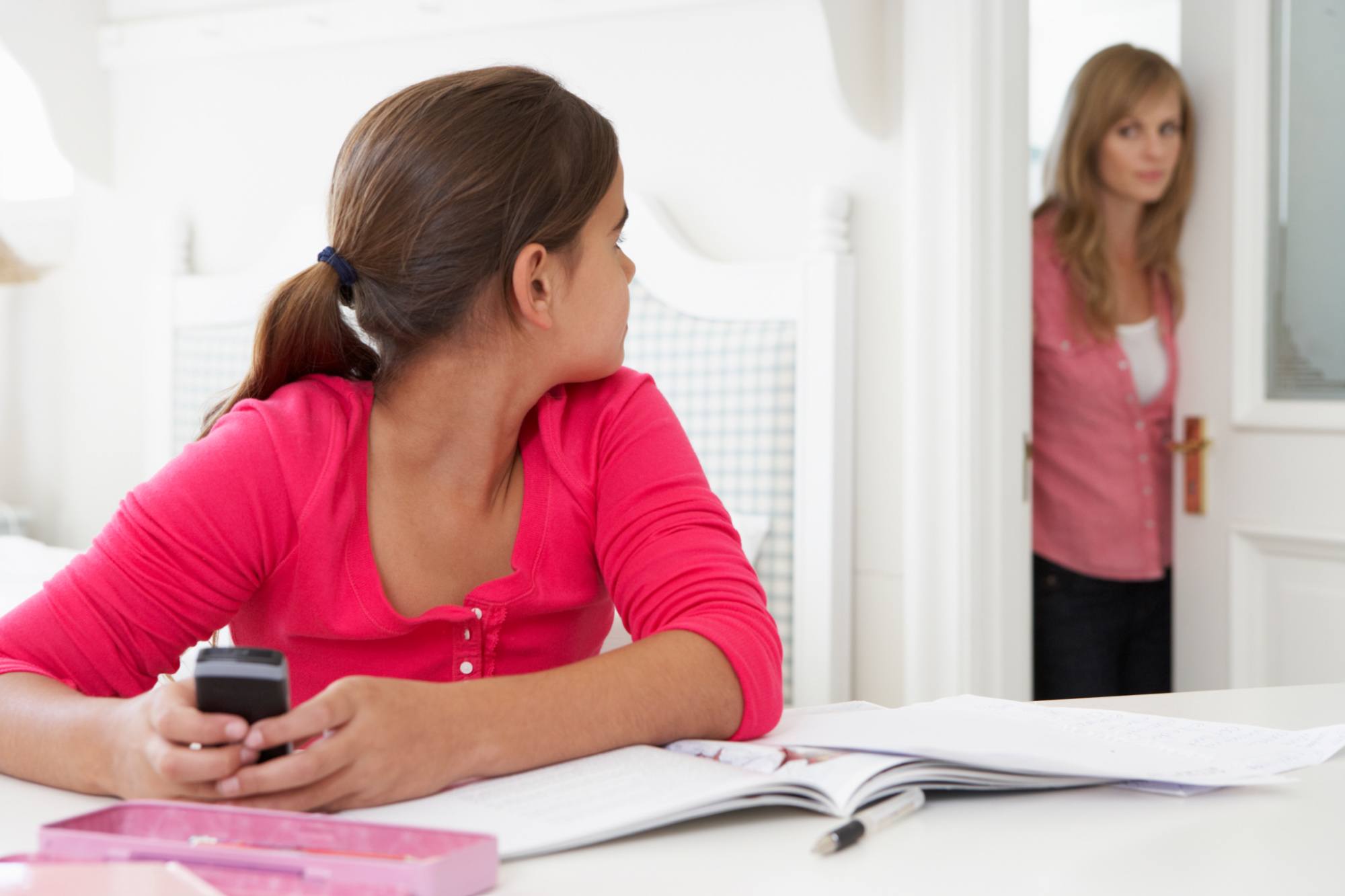 Girl with phone looking guilty at her mother who is looking in through the door.