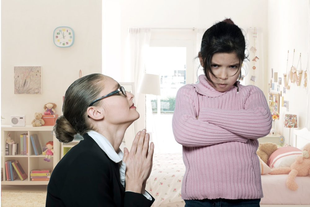 Mother on her knees begging child who is scowling with arms crossed.