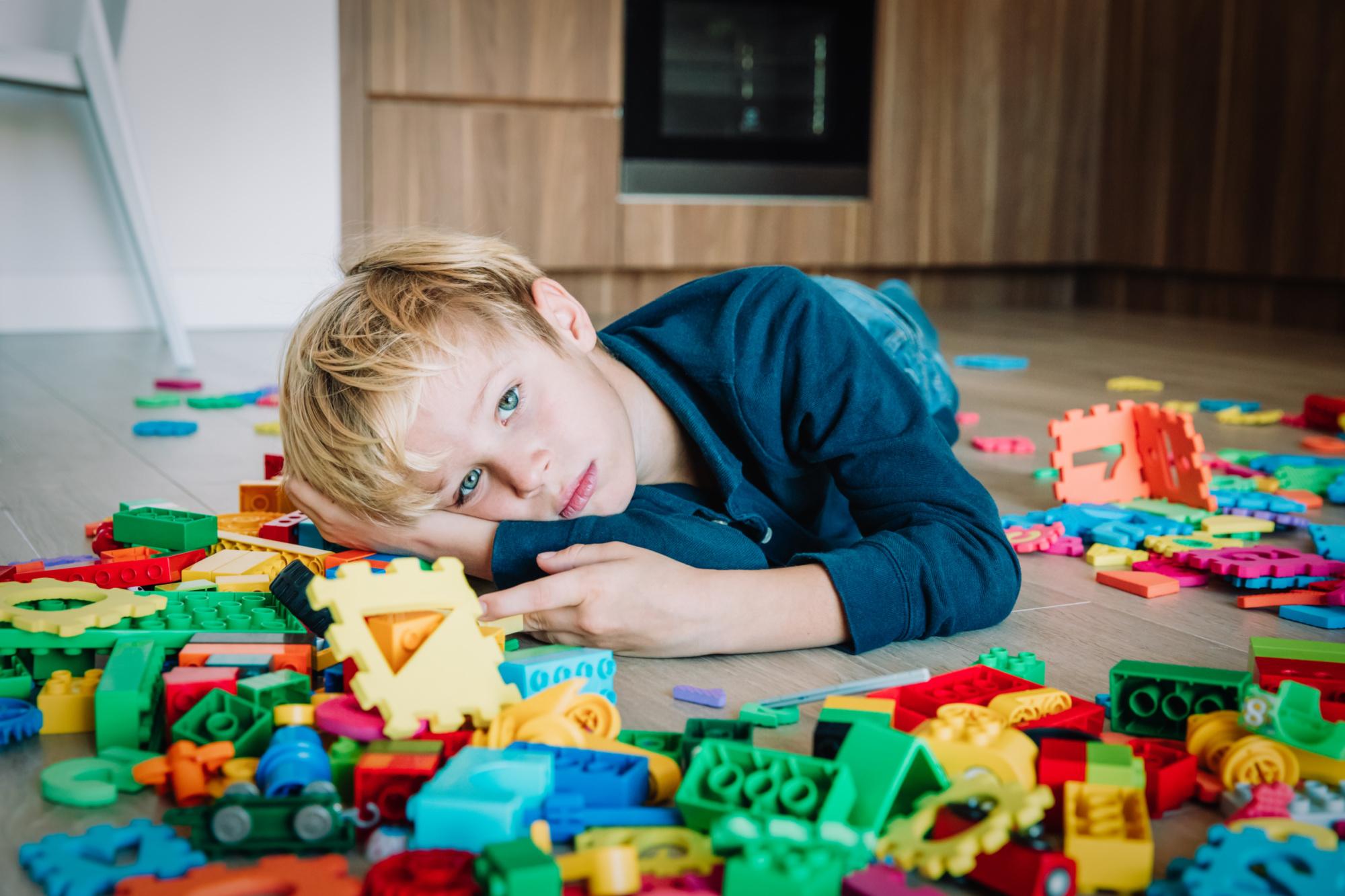 Sad boy lying on floor amidst toys.