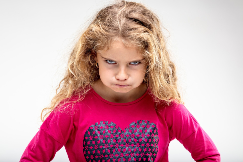 Portrait of preteen sulky girl making angry face against plain background