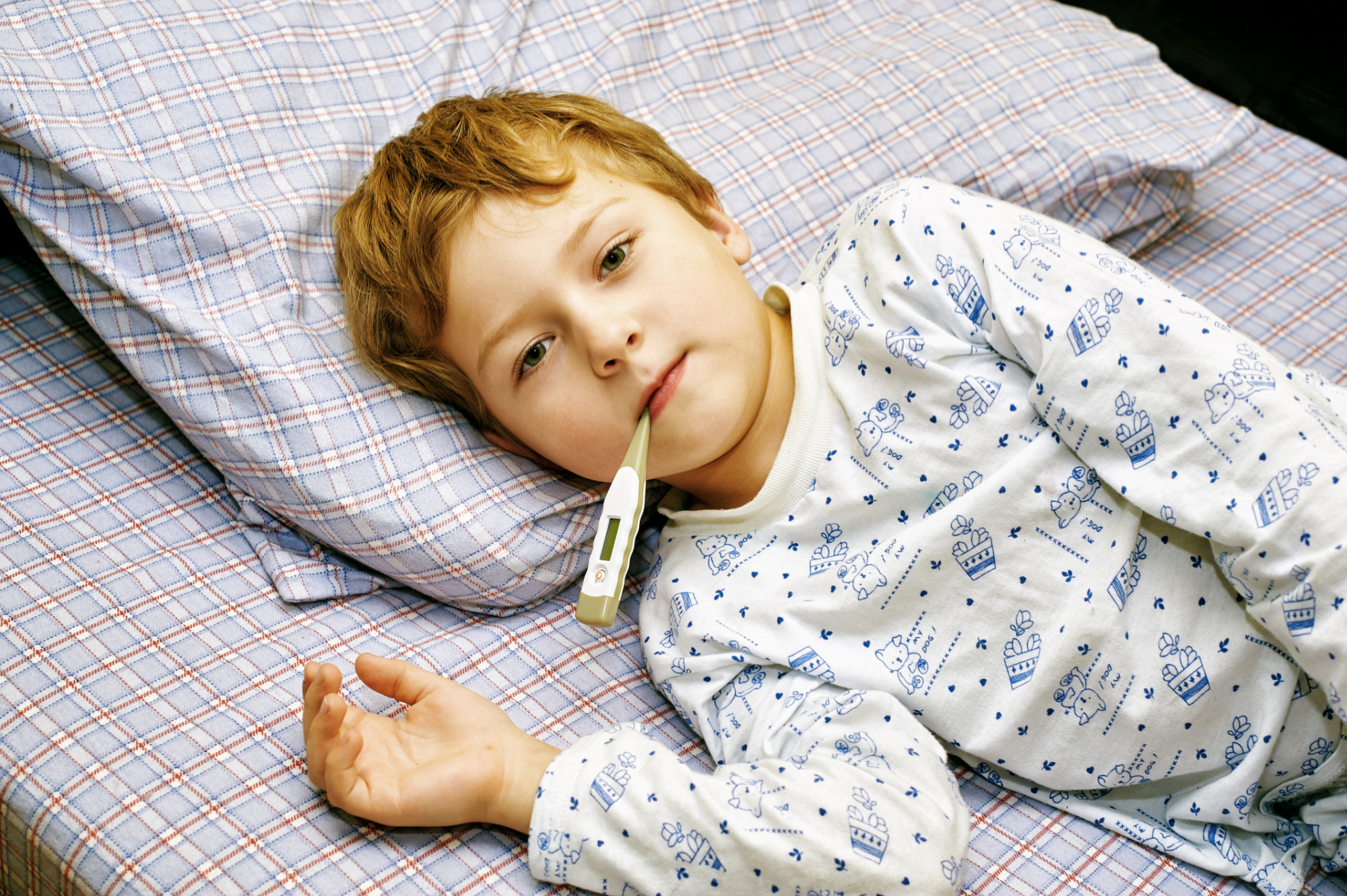 Young boy lying in bed with a thermometer in his mouth.