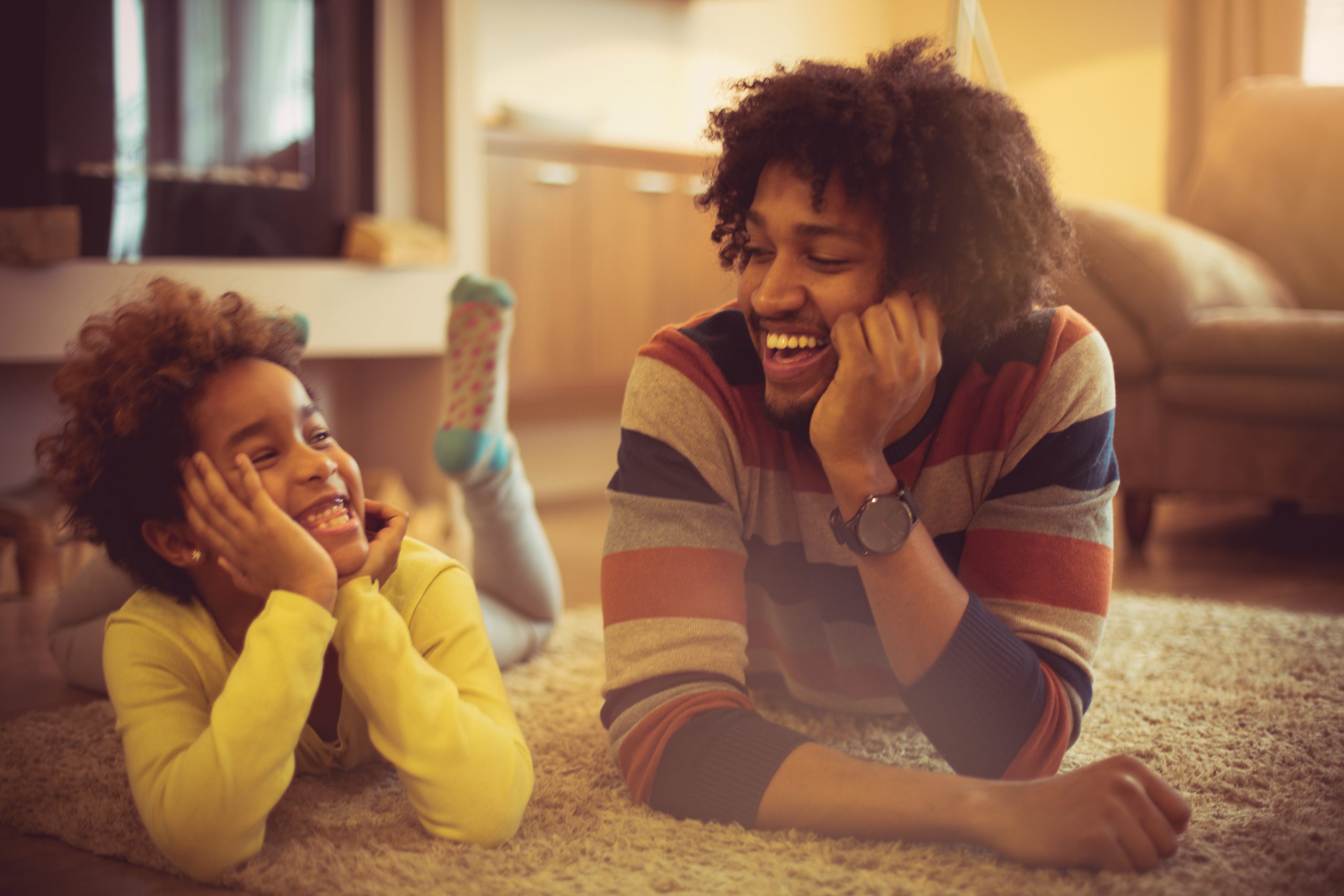 Father and daughter lying on the floor laughing together.